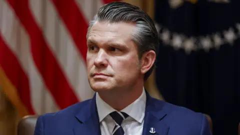 Pete Hegseth, wearing a blue suit, blue and white striped neck tie and a lapel pin, during a meeting at the White House.