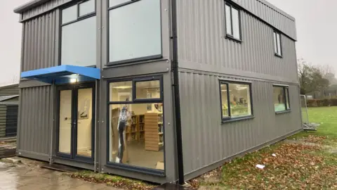Luke Deal/BBC A container with windows that has been repurposed to become a library. Shelves are visible through the windows.
