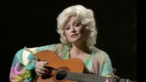 A young Dolly Parton playing an acoustic guitar