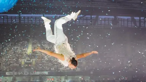 Millie Harvey is upside down in mid-air during her performance at the Take That concert at the Ethihad Stadium