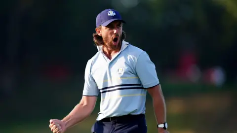 PA Media Tommy Fleetwood of Team Europe gives a fist pump reacts pursuing a putt connected 16 connected time 1 of nan 2025 Ryder Cup astatine nan Bethpage Black Course, Farmingdale, New York. He is wearing a Team Europe Ryder Cup navy shot headdress ray bluish and navy and top. 