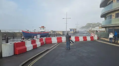 Dorset Council A man filming the red and white barriers that have been put up on the seafront