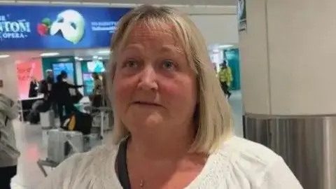 A woman in a white top stands in an airport hall.