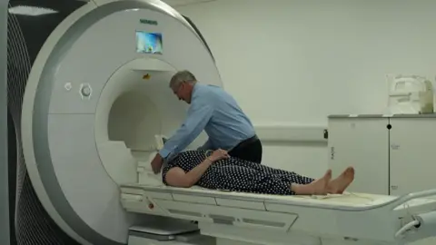 A doctor assists a patient about to go into an MRI scanner.