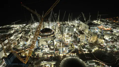EDF/PA Wire A night-time drone shot over the nuclear station construction site with many cranes and partially built sites brilliantly lit up against a black sky.