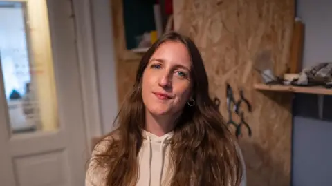 Chris King Rebecca smiling while stood in home near door and blue wall.