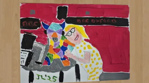 Jamie Lee Matthias's painting of BBC Radio Oxford's Sophie Law cuddling a colourful ox in the BBC Oxford radio studio.