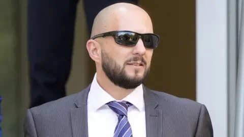 Det Insp Mark Portelli outside Southampton Magistrates' Court. He is completely bald with a dark beard. He wears sunglasses, a pinstripe grey suit and a striped blue tie.