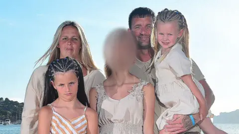 Submitted Man and woman hold three children who have their faces blurred