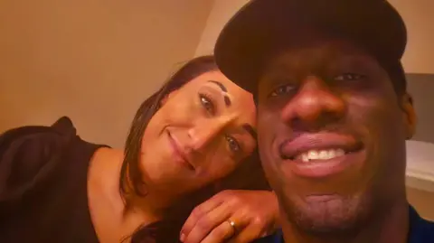 Salma Shah A woman is resting her hand on a man's shoulder, you can see she has an engagement ring on. Both are smiling in the selfie photo.