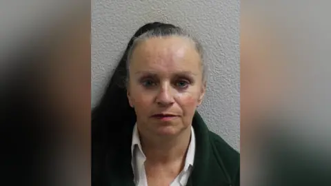 Metropolitan Police Custody image of Tina Smith, wearing a dark jacket and white shirt, photographed against a plain wall.