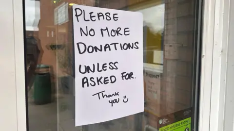 A glass door with a white piece of paper on it. It reads "please no more donations unless asked for. thank you"