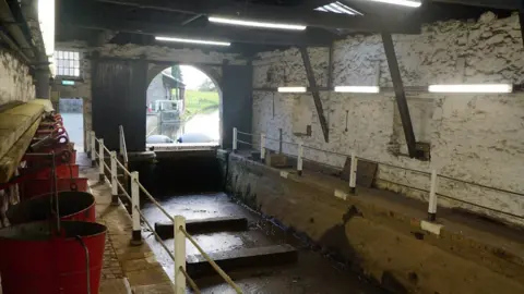 Ian Roberts The photo shows inside a building where boats are worked on with a low ceiling and old stone whitewashed walls