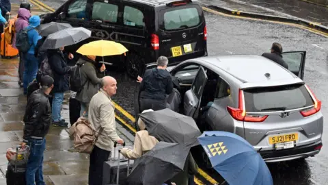 Getty Images A taxi and a private hire car dropping people with umbrellas off in Edinburgh on a rainy day.