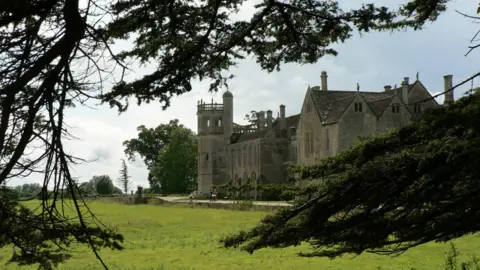 A view of Lacock Abbey on a sunny day, looking through the branches of a large tree