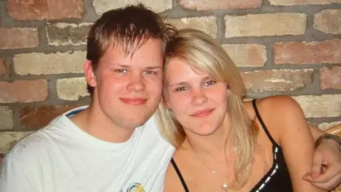 Tom Foddy Tom and Samantha Foddy, both looking at the camera and smiling. Tom has his arm around Samantha and they are leaning into each other. Tom has short fair hair and Samantha long blonde hair. Tom is wearing a white T-shirt and Samantha a black top. She has a necklace round her neck. 