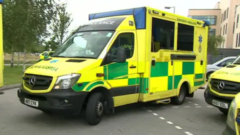 An ambulance pulls out of a parking space. It is yellow and green.