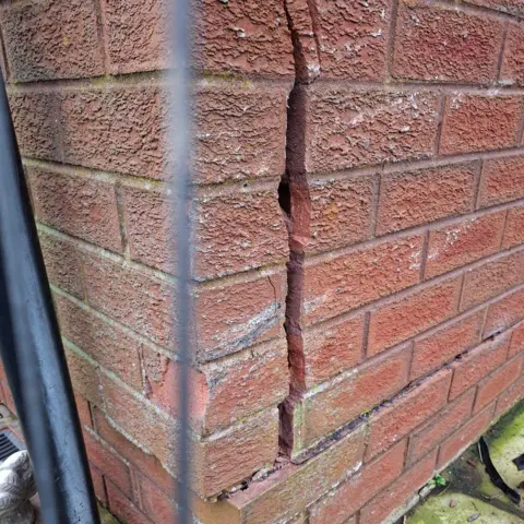 Thomas Kyle A closeup of a a redbrick wall. A large crack can be seen down it.