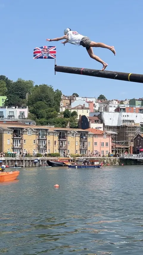 A man is launching off a pole into the water below.