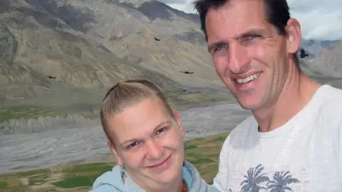Claire Boyd and Kevin Boyd smile and pose together against a mountainous backdrop. 