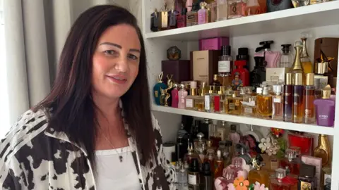 A woman with a long dark brown hair wears a cow printing jacket standing in front of a perfume show