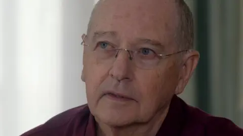 BBC/Chatterbox Media A man with rimless glasses, blue eyes and grey hair and wearing a burgundy shirt.