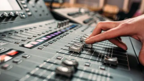 A person's hand moving sliders on a professional high-end sound mixing desk.