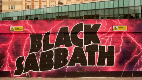 John Bray Part of a mural in Birmingham city centre with Black Sabbath in black letters on a neon pink background with streaks of lightning
