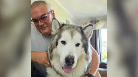 Robert Catchlove A fluffy malamute dog and a man look at the camera 