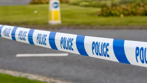 Stock image of a scene of a crash, with a police cordon in front of a road