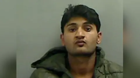 Mugshot of Haider Ali, a young man with dark hair, a faint moustache and a serious expression.