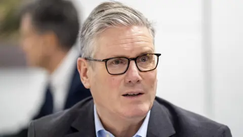 Sir Keir Starmer wears a dark grey suit and pale blue shirt.