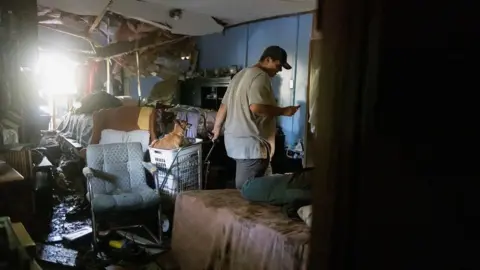 Reuters A man walks through a room which has its ceiling falling down and furniture damaged