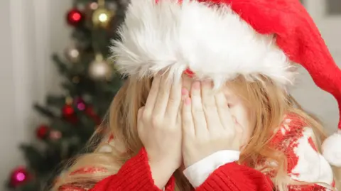 Getty Images Sad, frustrated little girl in Christmas outfit and Santa hat