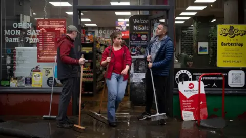 Staff with brooms clear water and mud from entrance to shop