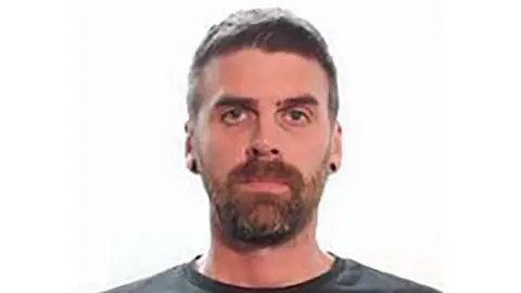 A police mugshot of Christopher Malcolm, a man with a beard looking at the camera.