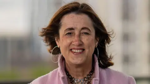 A woman with brown hair and a pink coat, Jane Dodds, smiling