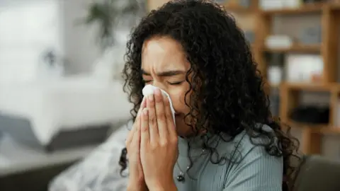 Woman sneezes into a tissue