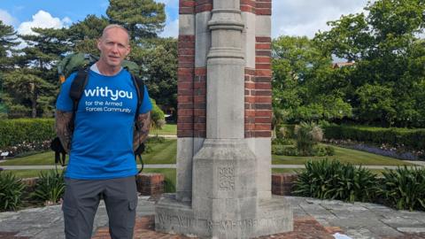 Jay Campbell, from Bournemouth stood by a war memorial in a blue t-shirt which says with you