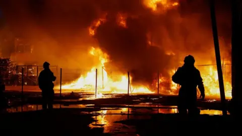 Two rescuers are silhouetted against a backdrop of fire in Kyiv