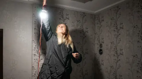 Matthew Goddard/BBC Yulia hangs a light in her home