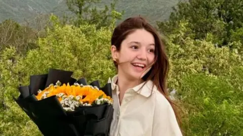 A teenage girl smiles while holding a bouquet of flowers