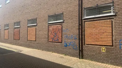 Brown brick building with graffiti on it saying 'no more boats' in blue paint 