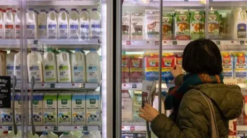 As imagens cartas chegaram a uma geladeira de supermercado para escolher uma caixa de um leite feminino.