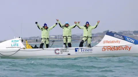 Row for Life Three women stood on a row boat off the coast of Dorset.