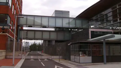 Seth Whales The image shows two glass walkways connecting the red brick Tŷ Hywel building on the left and the Senedd building on the right.