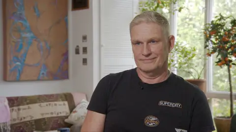 Philip Hurd, seorang pria dengan rambut berwarna terang mengenakan T-shirt hitam dengan logo superdry