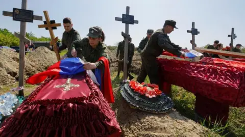 Reuters: A number of Russian soldiers hang flags on the coffins of soldiers who were killed in Luhansk, a region controlled by Russia, surrounded by crosses.