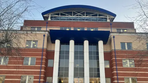 Nadia Lincoln A red brick building with a glass entrance and four white columns at the front of the structure. 