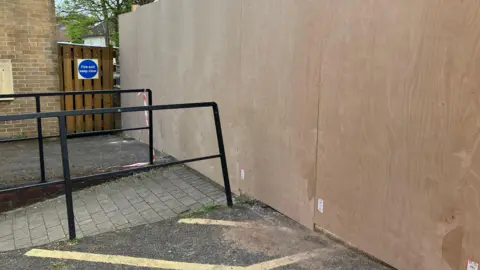 A large wooden wall put in a car park, with a very small gap left for the disabled access ramp